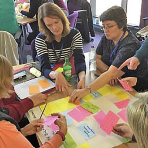 A group of people sit around a table placing, pointing at and discussing post-its