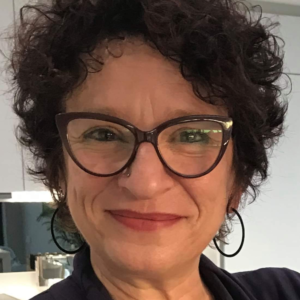 The head of a woman facing the camera. She has curly hair and wears glasses