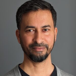 The head of a man facing the camera. He has short dark hair and a dark beard