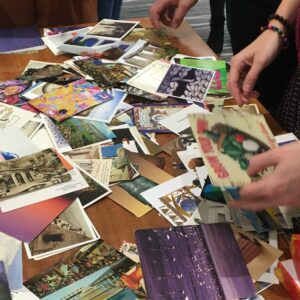 A table covered in old postcards. A hand is reaching to pick one card up