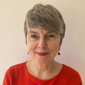 The head of a woman facing the camera. She as short hair and wears an orange top