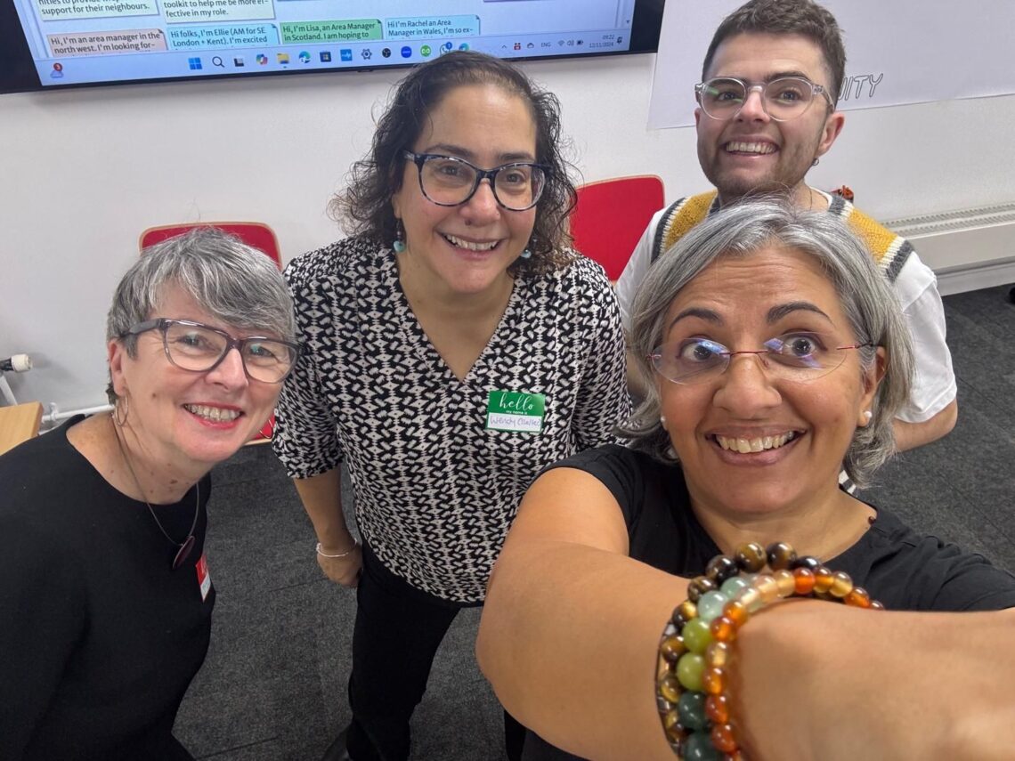 Four people smiling at the camera. One holds the phone out to take a selfie.