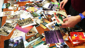 A tabletop covered in old postcards during a Train the trainer session. Several hands reach in, each picking up a card.
