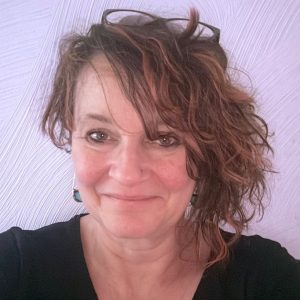 The head of a woman looking straight at the camera. She has shoulder length hair and is wearing black.